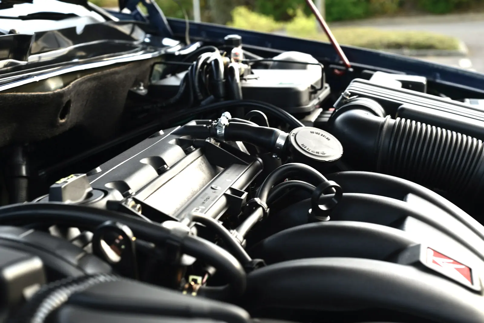 Engine bay of a parked car with black rubber hoses held to their fittings by metal clamps, beside a ribbed air intake duct.