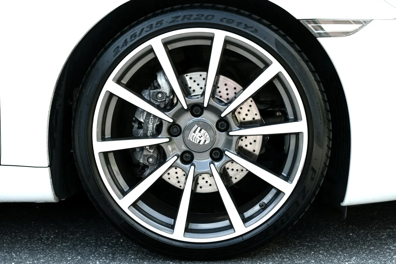 A ten-spoke alloy wheel on a white sports car, with a large drilled brake rotor and caliper visible close behind the spokes.
