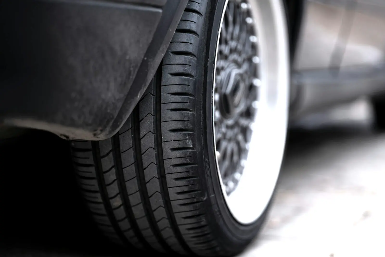 Low-angle close-up of a lowered car's rear tire and polished-lip mesh wheel sitting just inside the edge of the fender.