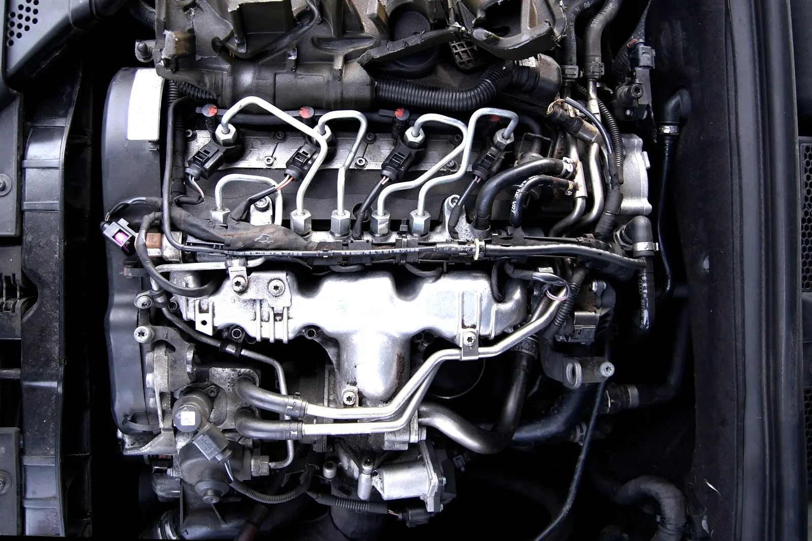 A four-cylinder diesel engine in a car's engine bay, with steel high-pressure fuel lines running from the common rail to each injector.