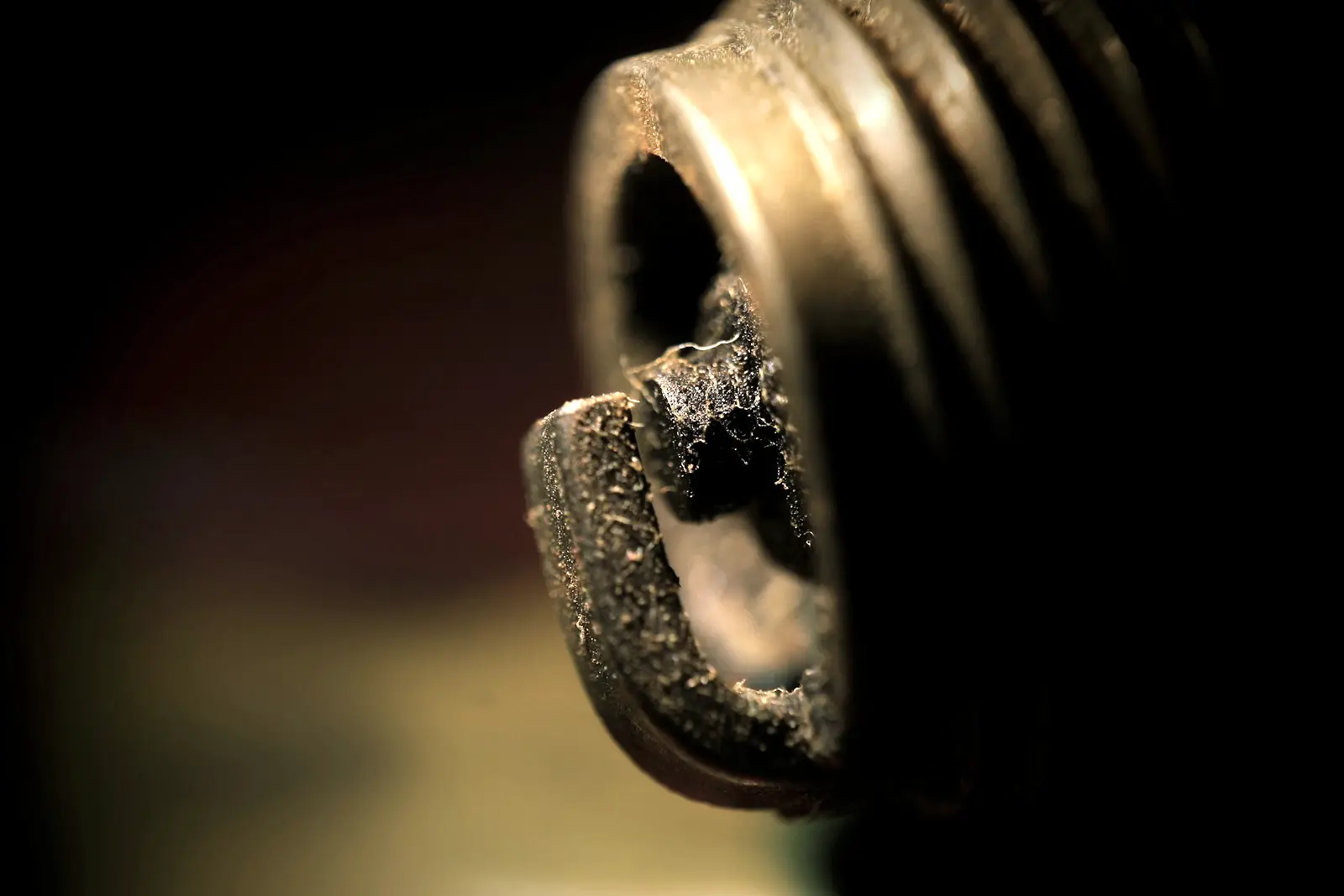 Macro view of a used spark plug tip, the electrode and threads crusted in black carbon deposits.