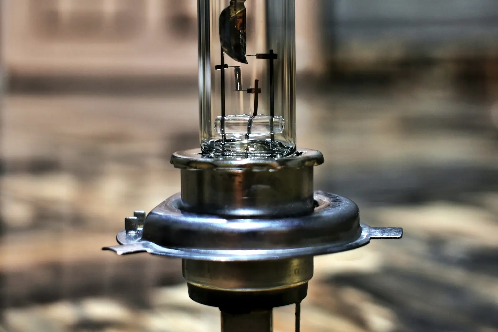 A single H4 halogen headlight bulb standing upright, its clear glass capsule showing the filaments above a metal mounting flange.