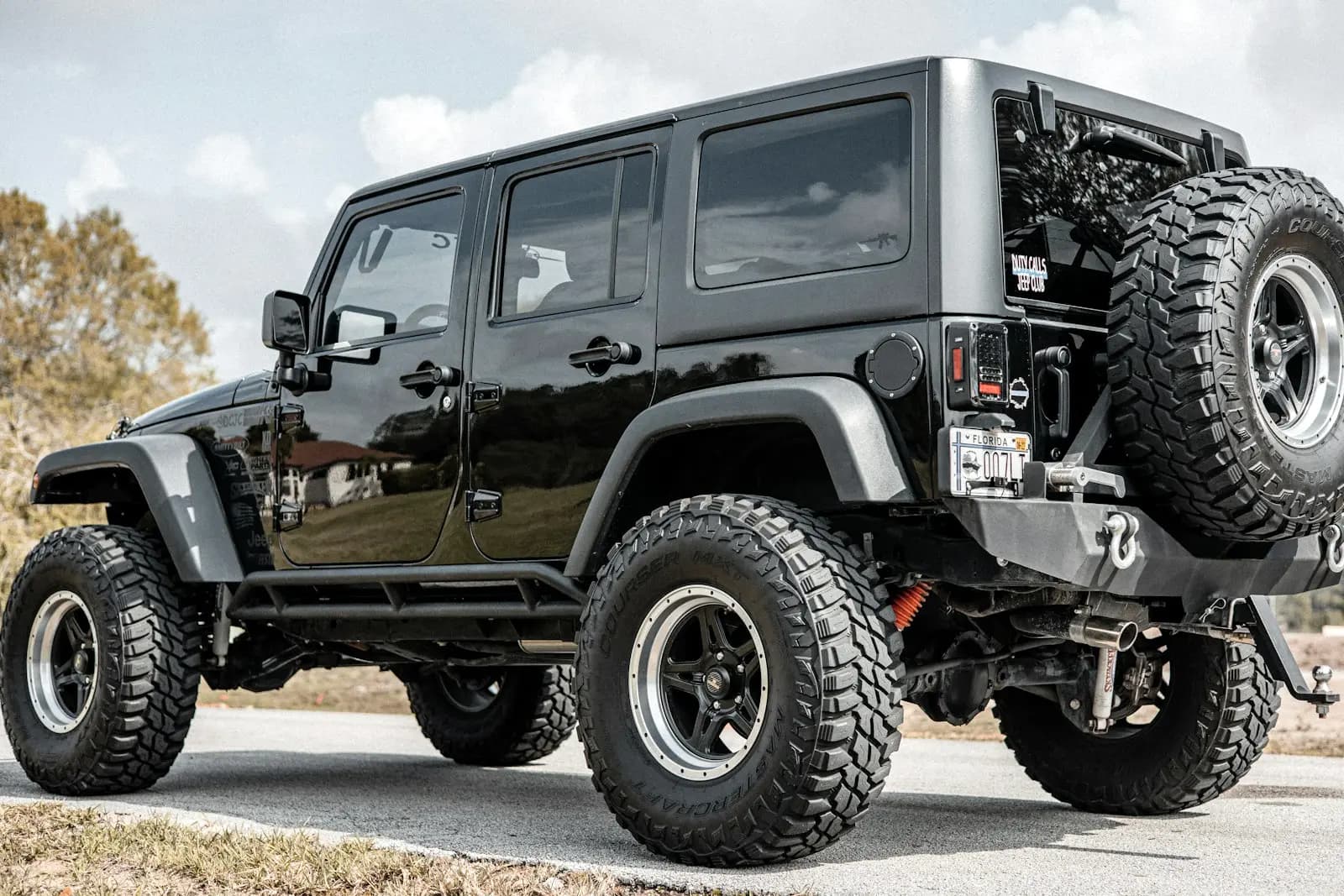 Rear three-quarter view of a lifted black four-door SUV on oversized mud-terrain tires, with a matching spare mounted on the tailgate.