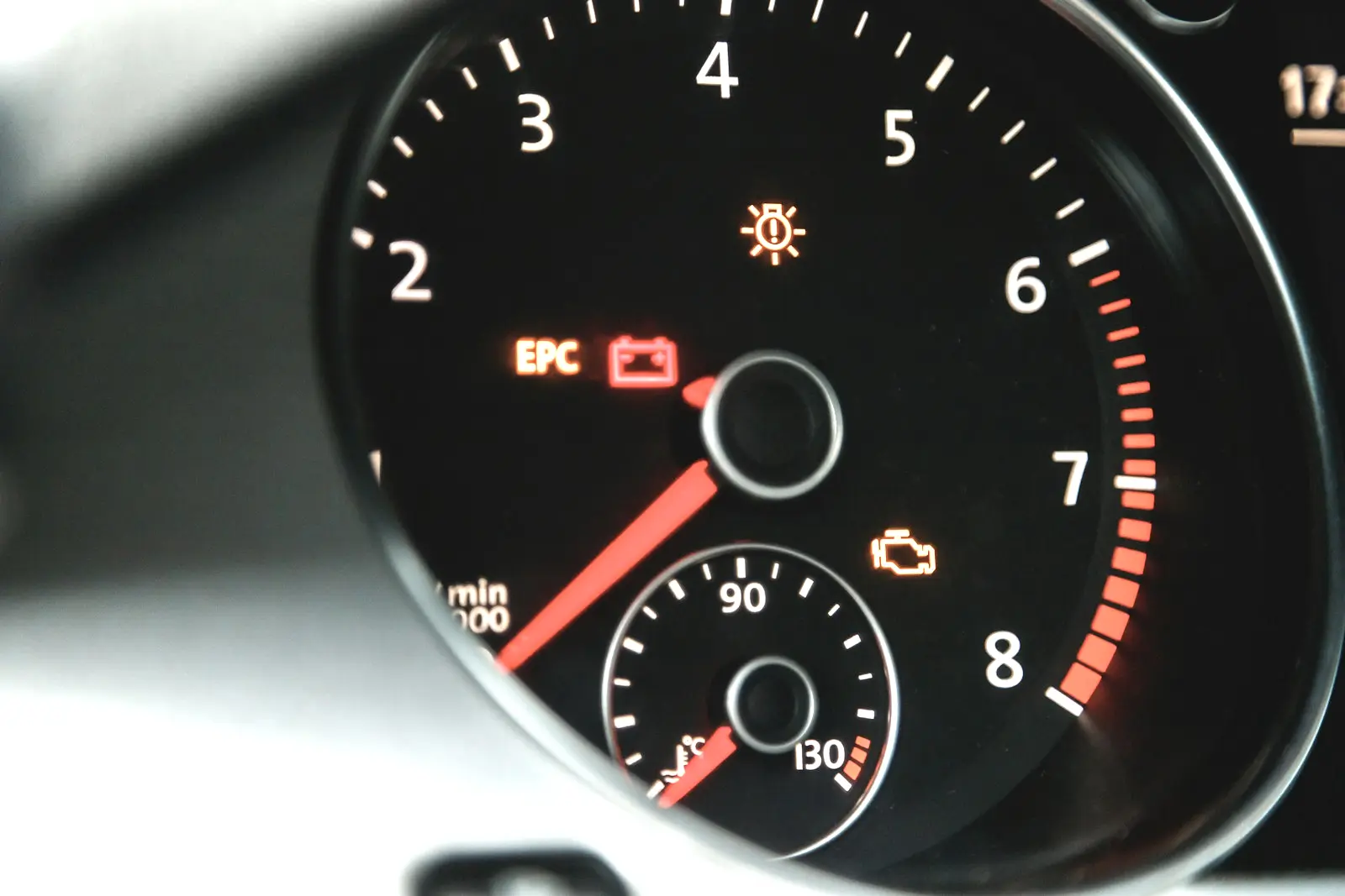 A car tachometer with several warning lamps lit, including the amber check engine symbol below the needle hub.
