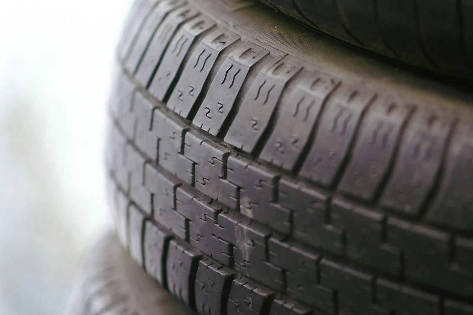Close-up of the tread face of a passenger car tire in a stack, showing rows of tread blocks and sipes against a pale background.