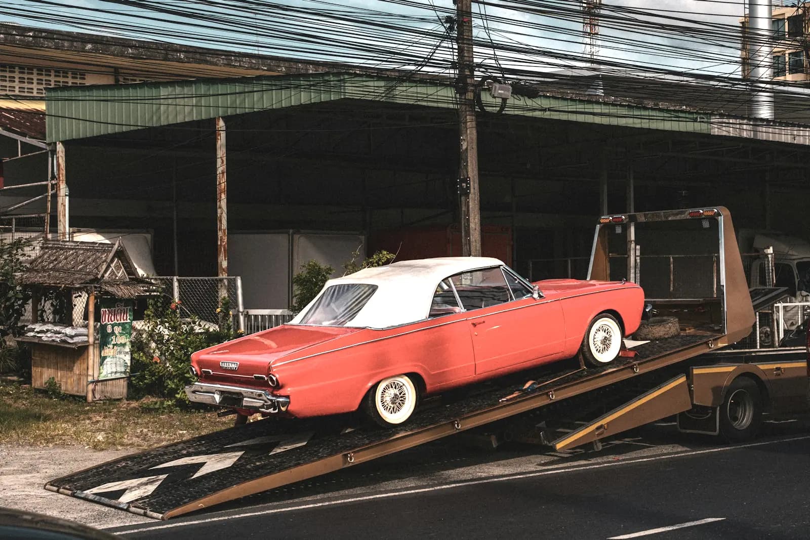 Red classic convertible sitting on the tilted bed of a flatbed tow truck, all four wheels on the deck.