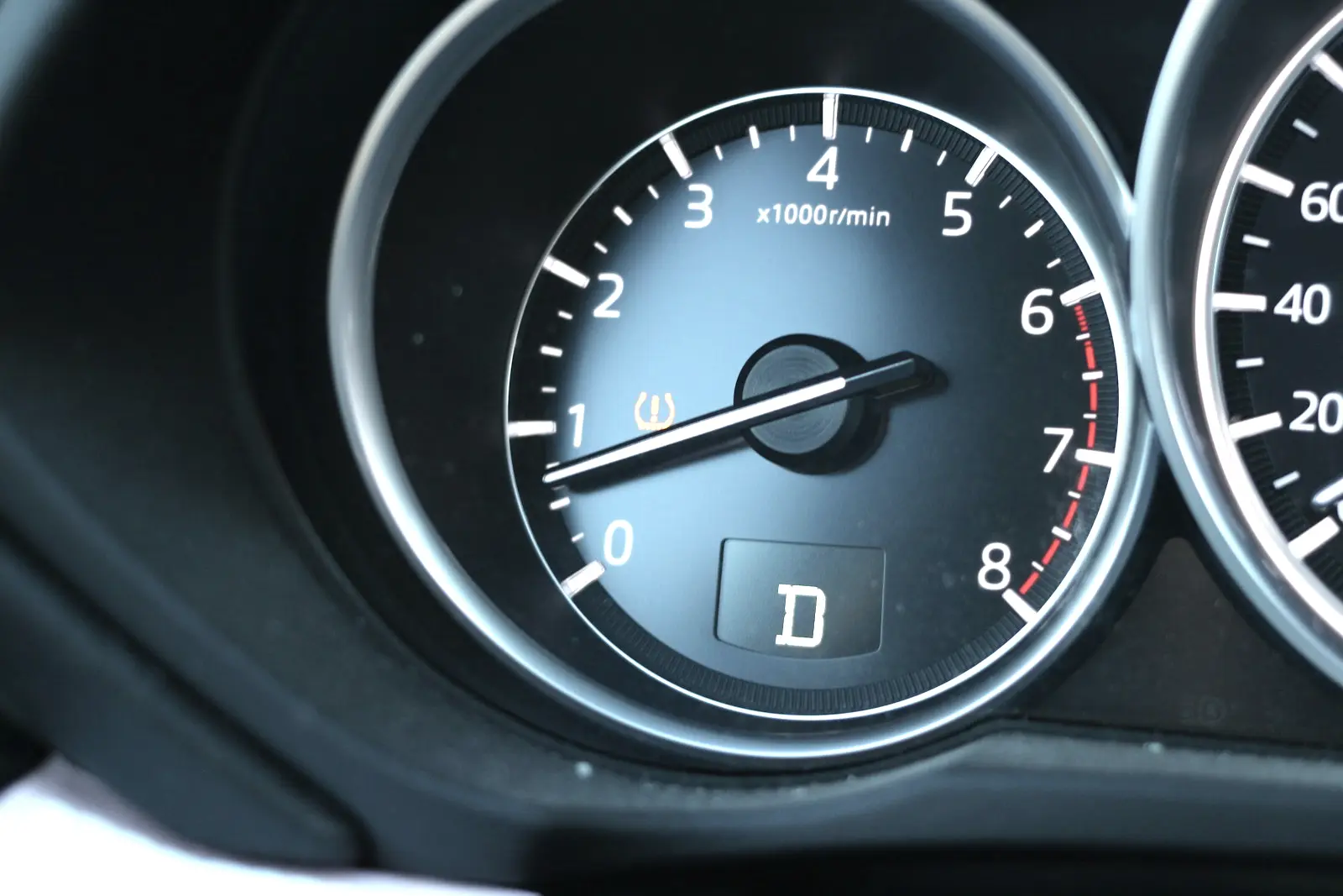 A car's tachometer with the amber tire pressure warning symbol lit inside the dial, and the gear indicator showing D.