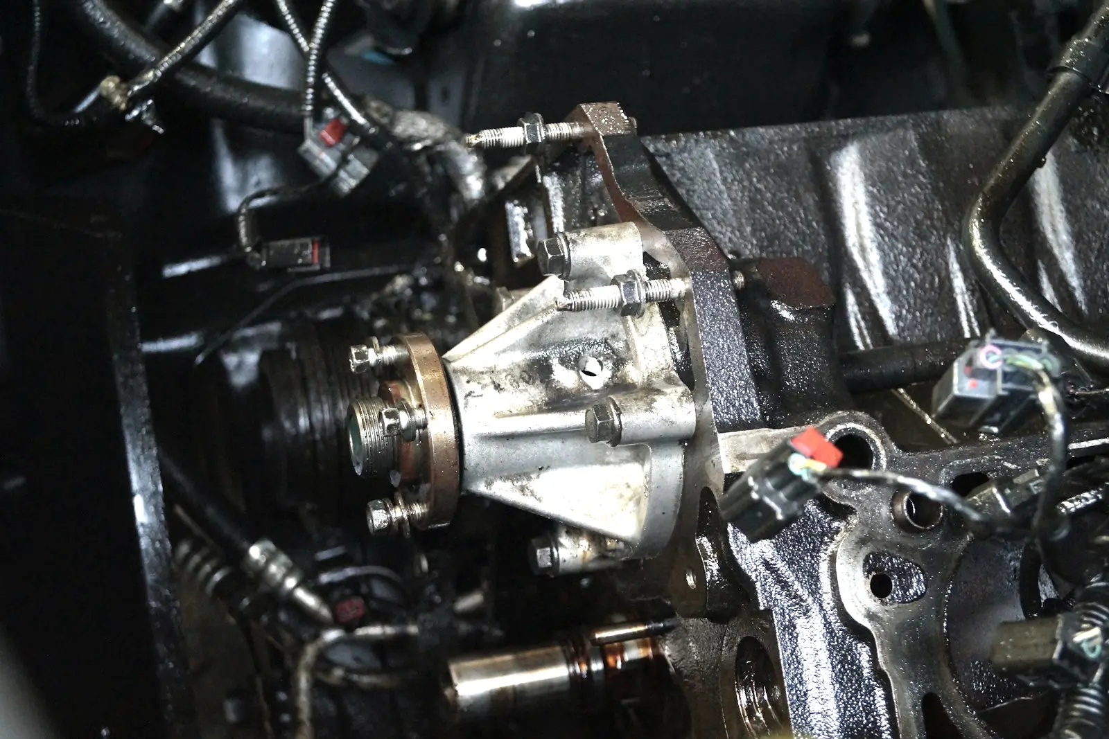 Water pump bolted to the front of an engine block with its pulley removed, the housing stained with dried residue around a small hole.