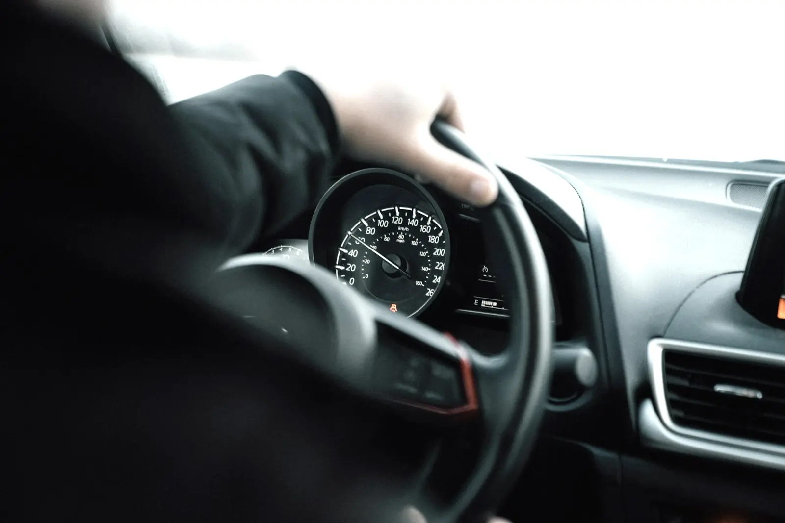 Driver's hand on the steering wheel at road speed, with the speedometer visible through the wheel.